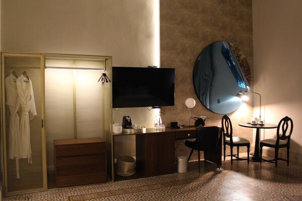 Una habitación de hotel con cama, escritorio con televisor, espejo y una pequeña mesa con sillas.