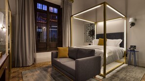 Una habitación de hotel moderna con una cama con dosel, un sofá, una mesita y un ventanal con cortinas.