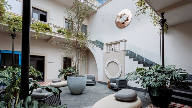 Un patio interior moderno con zonas de estar, plantas en macetas y una escalera.