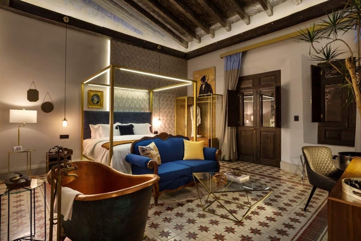 A room with a four-poster bed, a blue sofa, a vintage bathtub, and a star-patterned floor.