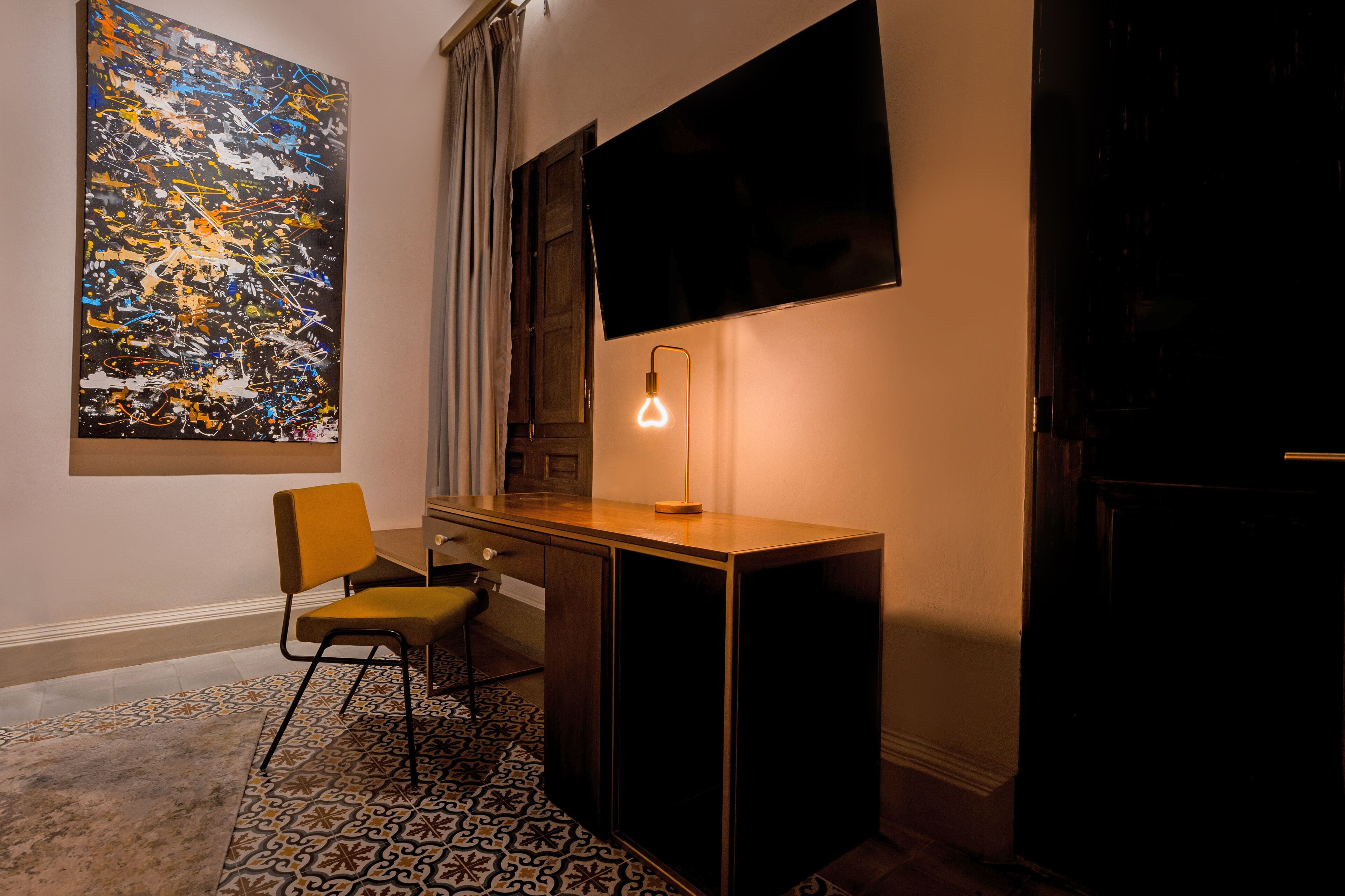 A room with a desk, a chair, a large abstract painting, a flat-screen TV, and a patterned rug.