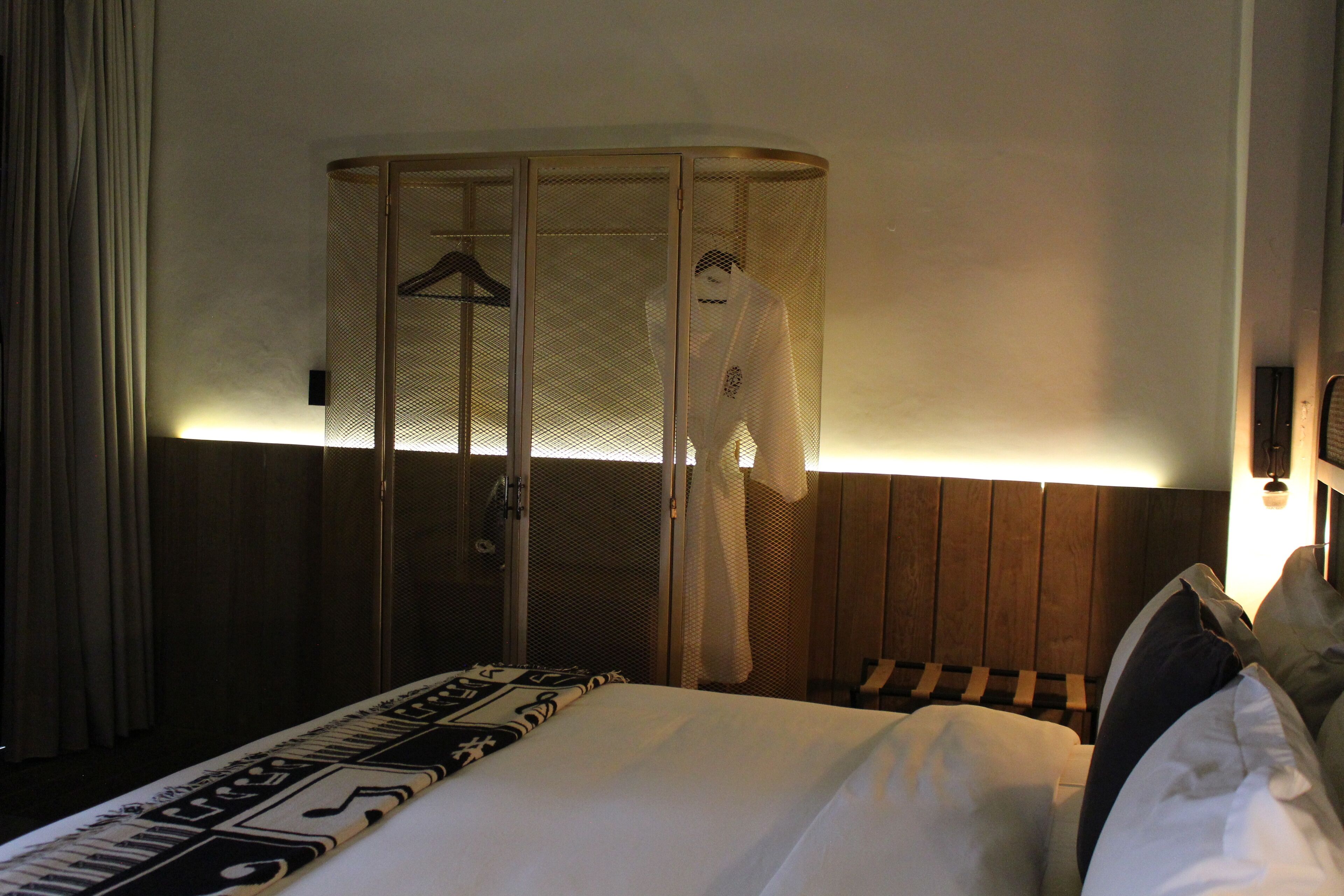 A hotel room with a bed, a hanging robe, and a wooden headboard.