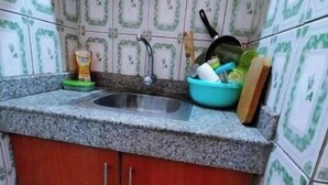 Ett litet kök med en bänkskiva i granit, en diskho och ett träskåp. På bänkskivan finns olika köksredskap, bland annat en grön skål, en stekpanna och en skärbräda.