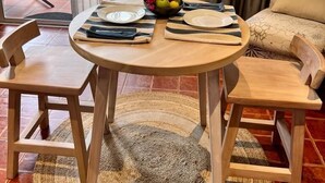 Ein runder Holztisch mit einem gewebten Teppich, zwei Holzstühlen, einer Obstschale und einem Essensset.