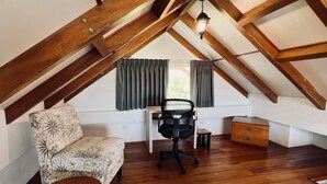 Ein Schlafzimmer im Loft-Stil mit schrägen Wänden, Holzbalken, einem Schreibtisch, einem Sessel, einer Couch und einer kleinen Holzkiste.