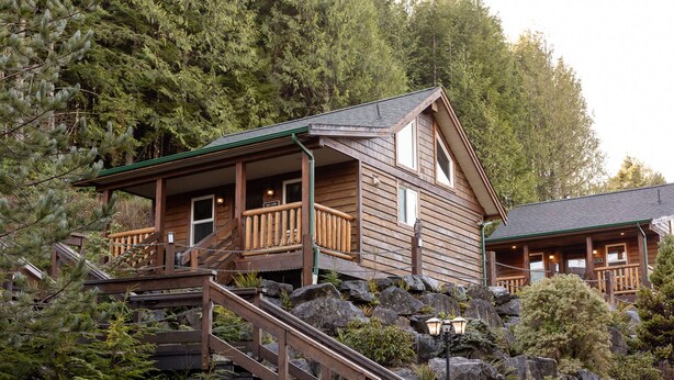 Eine Holzhütte mit Balkon, umgeben von dichtem Wald und felsigem Gelände.