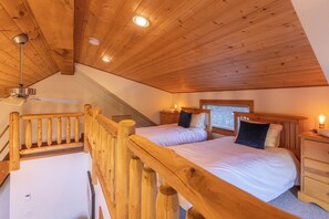 A bedroom with two beds, wooden ceiling beams, a ceiling fan, and a window with blinds.