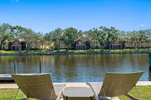 A view of a lake with two wicker chairs facing it, surrounded by trees and buildings in the background. - NEW Heated Salt Pool & Spa on Waterfront Canal (Tampa)