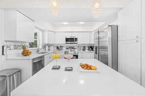 Una cocina moderna con armarios blancos, electrodomésticos de acero inoxidable y una isla central con bebidas y pasteles.