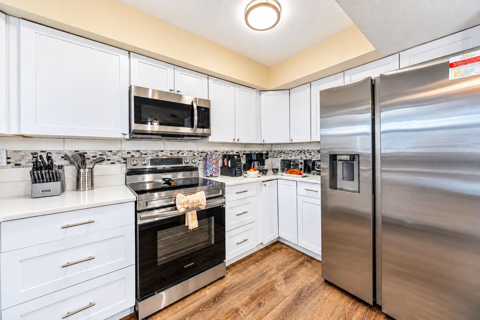 A modern kitchen with stainless steel appliances, white cabinetry, and a wooden floor.