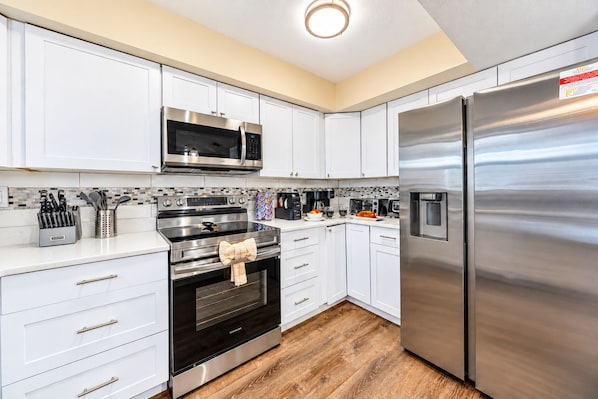 A modern kitchen with stainless steel appliances, white cabinetry, and a wooden floor. - NEW Heated Salt Pool & Spa on Waterfront Canal (Tampa)
