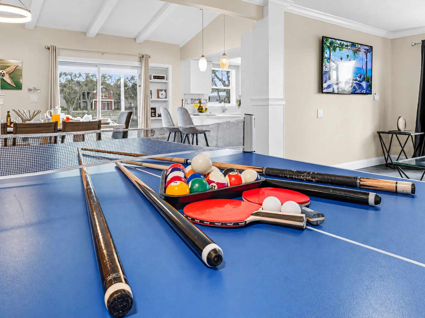 A pool table in a room with a dining area and a TV on the wall.