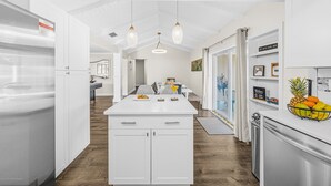 A modern kitchen with white cabinetry, a central island, pendant lighting, and a refrigerator on the right. - NEW Heated Salt Pool & Spa on Waterfront Canal (Tampa)