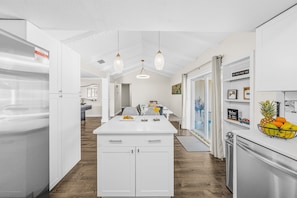 Una cocina moderna con armarios blancos, una isla central, iluminación colgante y un refrigerador a la derecha.