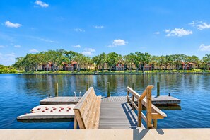 A wooden dock extending over calm water, leading to a small boat with red seats. - NEW Heated Salt Pool & Spa on Waterfront Canal (Tampa)