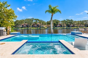 A swimming pool with a clear blue water feature, surrounded by a tiled deck and lounge chairs. - Waterfront | Heated Salt Pool & Spa (Tampa)