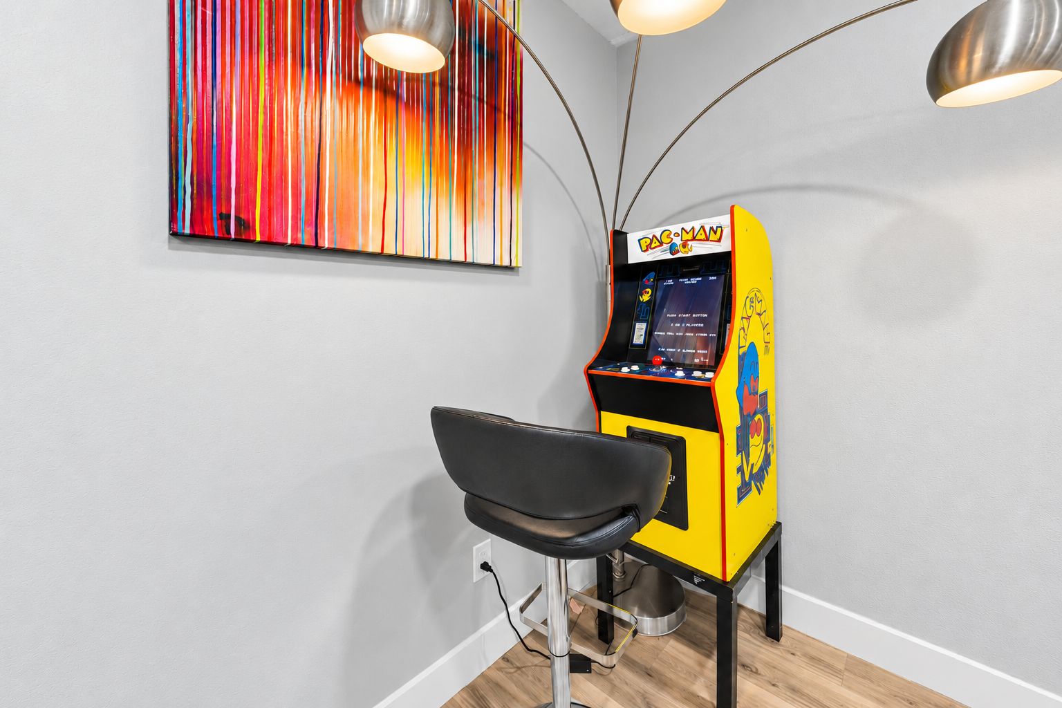 Una habitación con una máquina arcade de Pac-Man, una silla negra y un cuadro abstracto colorido en la pared.