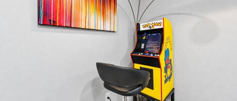 Una habitación con una máquina arcade de Pac-Man, una silla negra y un cuadro abstracto colorido en la pared.