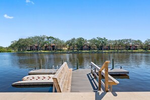 A wooden dock extending into a calm lake, surrounded by a row of buildings with a clear sky above. - NEW Heated Salt Pool & Spa on Waterfront Canal (Tampa)