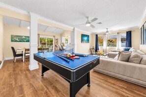 A pool table in a living room with a sofa and a dining area in the background. - NEW Heated Salt Pool & Spa on Waterfront Canal (Tampa)