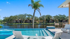 A swimming pool with a water feature, lounge chairs, and a view of a residential area with houses and a body of water. - NEW Heated Salt Pool & Spa on Waterfront Canal (Tampa)