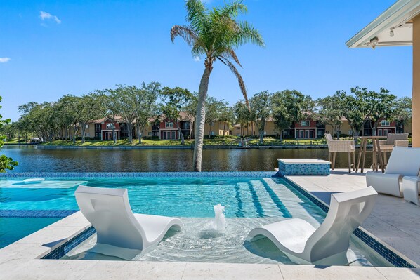 A swimming pool with a water feature, lounge chairs, and a view of a residential area with houses and a body of water. - NEW Heated Salt Pool & Spa on Waterfront Canal (Tampa)