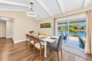 A dining area with a table set for four, a view of a swimming pool, and a painting on the wall. - NEW Heated Salt Pool & Spa on Waterfront Canal (Tampa)