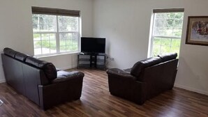 Ein Wohnzimmer mit zwei Ledersofas, einem Flachbildfernseher und großen Fenstern.