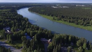 Ein Fluss schlängelt sich durch ein dicht bewaldetes Gebiet, entlang der Ufer sind einige Gebäude zu sehen.