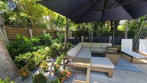 An outdoor patio with a wooden bench, a cushioned seating area, and a large umbrella.