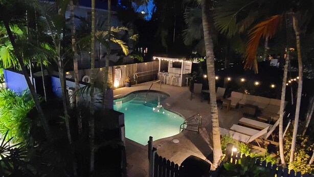 A swimming pool with a deck area, surrounded by palm trees and a fence.
