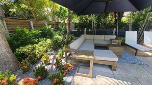 A patio with a wooden bench, a cushioned seating area, and a large umbrella. - Duval Street Suites full kitchen, free parking, & heated pool (Key West)