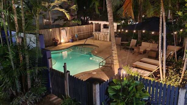 A pool area with a wooden fence, lounge chairs, and a bar. - Duval Street Suites full kitchen, free parking, & heated pool (Key West)