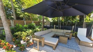 An outdoor patio with a sectional sofa, wooden coffee table, and a large umbrella. - Duval Street Suites with full kitchen heated pool, free parking (Key West)