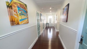 A long, narrow hallway with wooden floors and white walls, featuring a large colorful mural on the left and a door on the right. - Duval Street Suites with full kitchen heated pool, free parking (Key West)