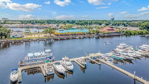 A marina with several boats docked, a large building with a green roof, and a water tower in the distance.