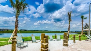 Eine Strandlounge mit Liegestühlen und Blick auf einen See, umgeben von Palmen und blauem Himmel.