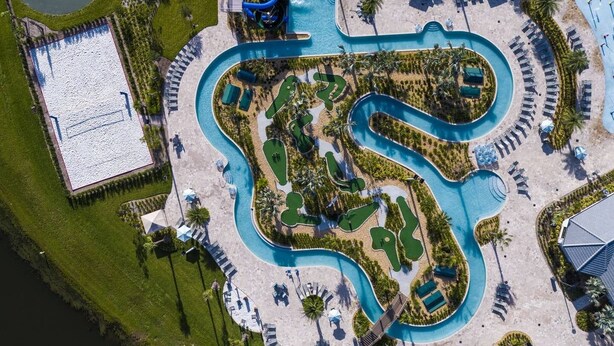 Eine Luftaufnahme eines Resorts mit einem gewundenen Pool, mehreren Liegebereichen und einem separaten Gebäude mit Pool.