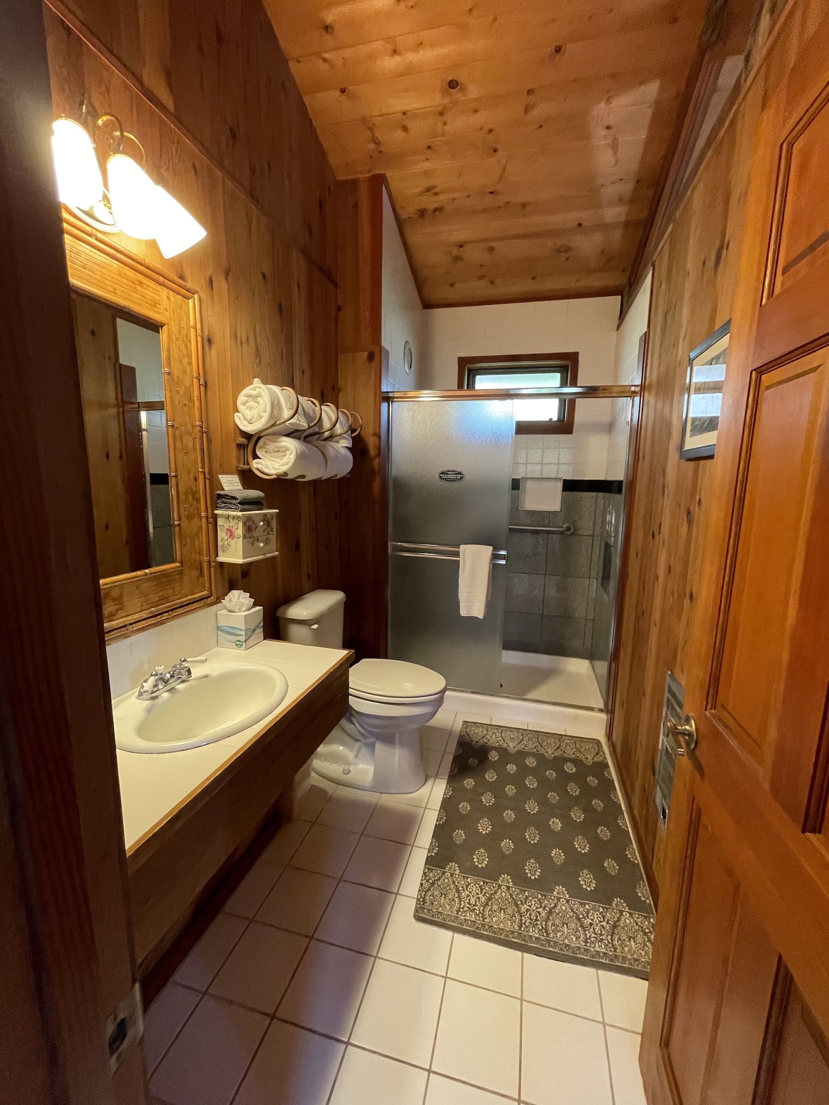 A wooden cabin bathroom with a sink, toilet, and shower.