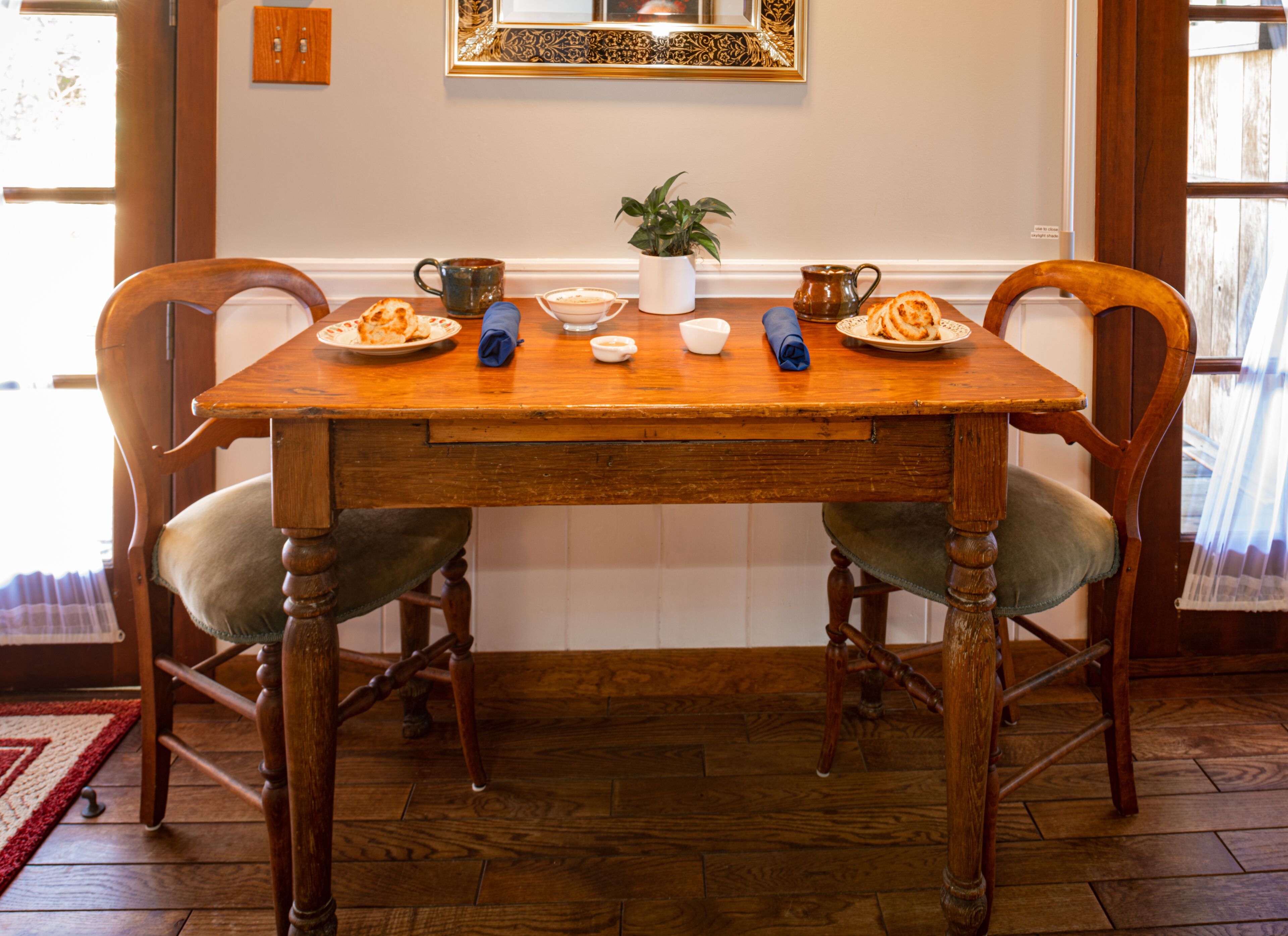 Une table de salle à manger en bois, avec des chaises, une plante en pot et des assiettes remplies de nourriture.