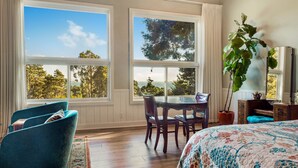 A room with large windows, a dining table, chairs, a bed with a floral bedspread, and a potted plant. - Rendezvous Mendocino (Gualala)