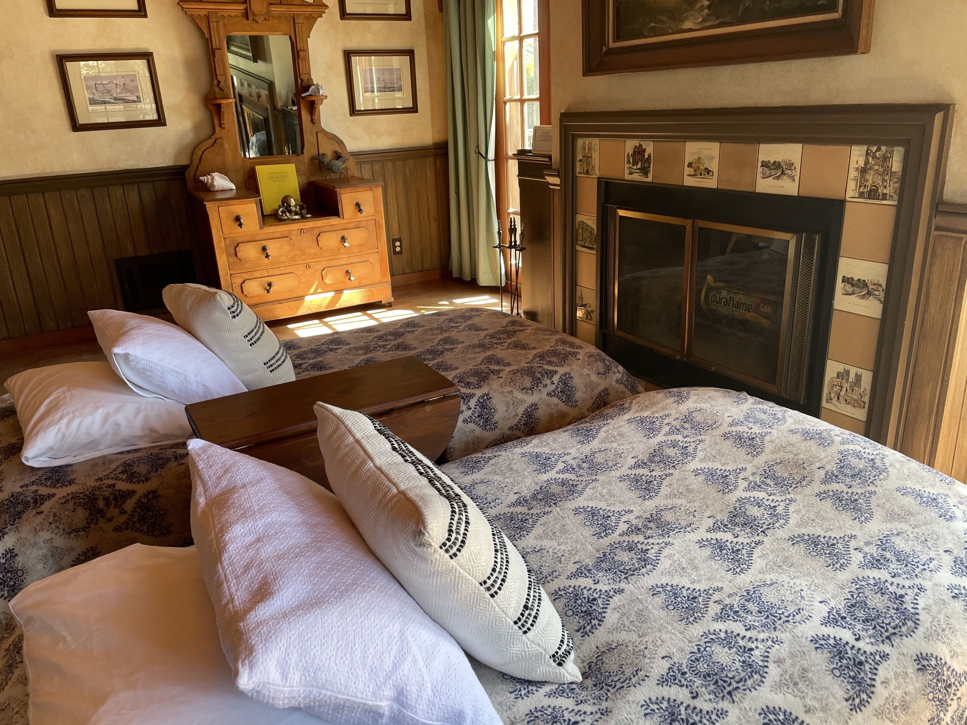 A bedroom with two beds, a dresser, a mirror, and a fireplace.