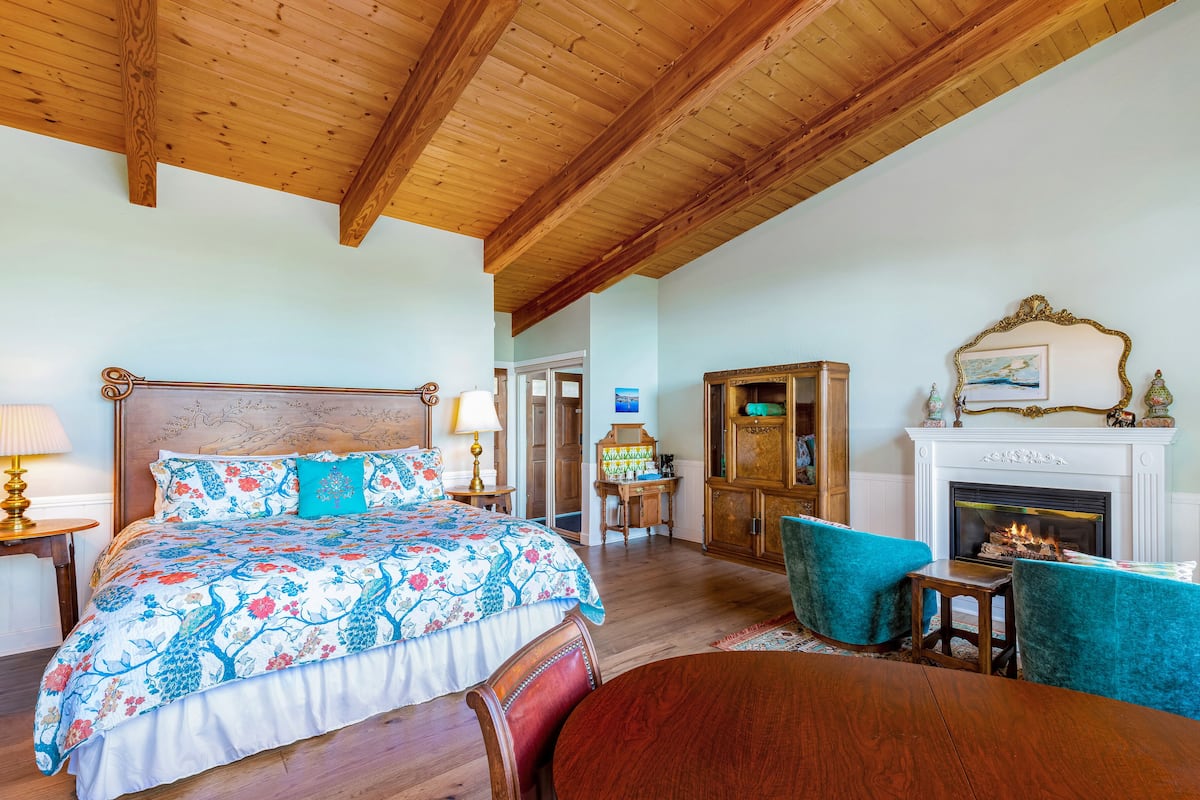 Un dormitorio con techo de madera, cama con ropa de cama floral, chimenea y un mueble de madera.