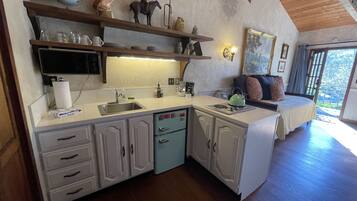 Cozinha com armários brancos, pia e fogão. Há uma prateleira sobre a pia com objetos decorativos.