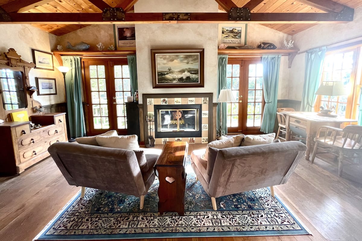 Una sala de estar acogedora con chimenea, dos sillones, una mesa de centro y techo de madera.
