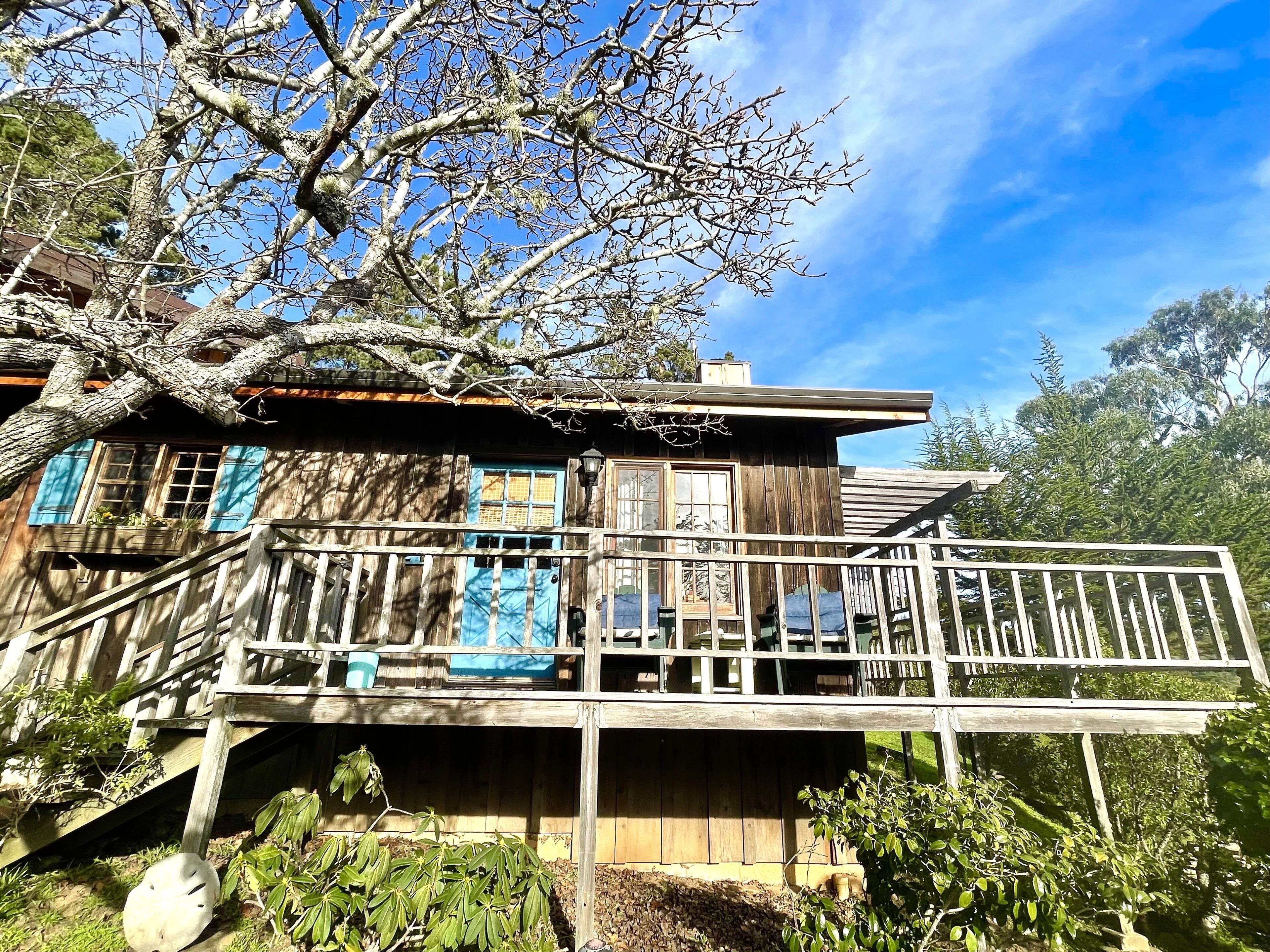 A rustic wooden house with a balcony, surrounded by trees and greenery.