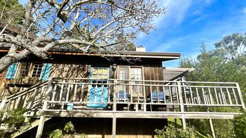 A rustic wooden house with a balcony, surrounded by trees and greenery.