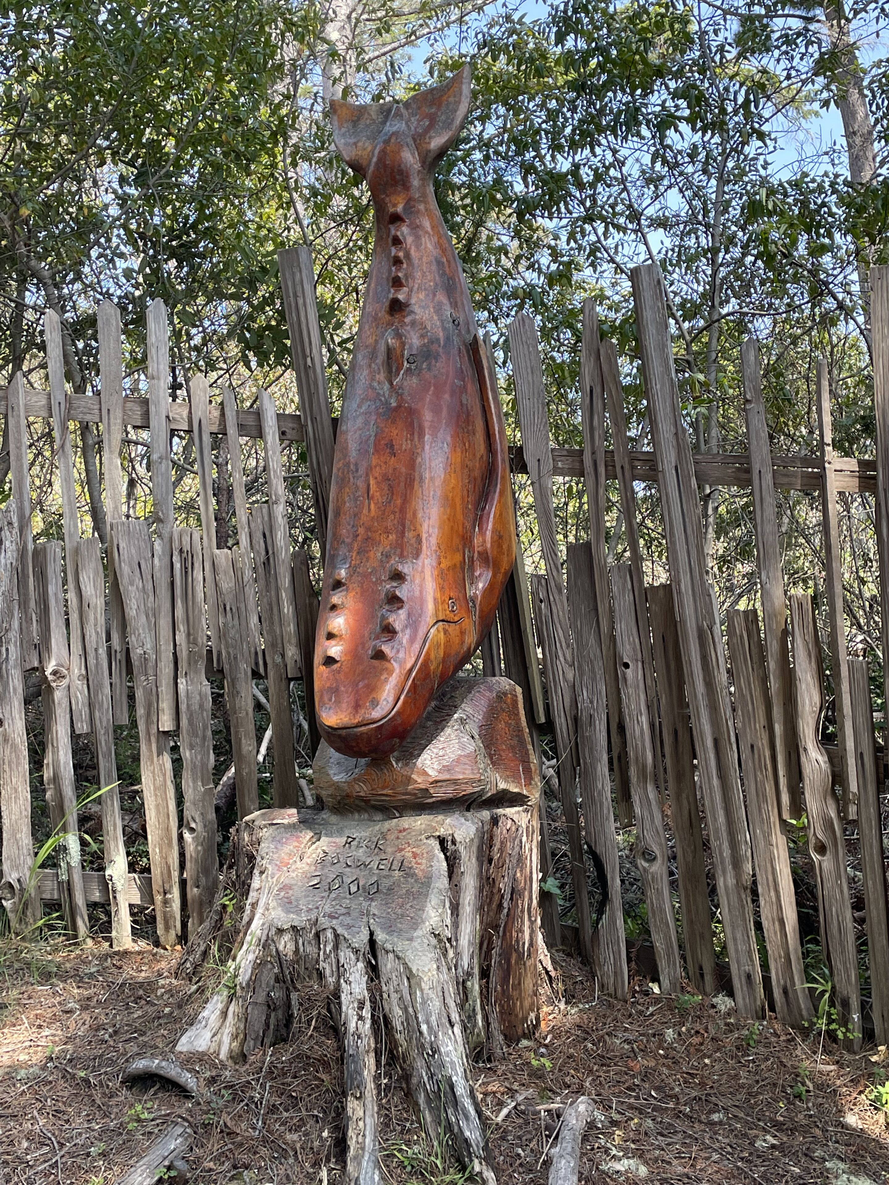 Una escultura de madera de la cabeza de un caballo montada sobre un tocón, rodeada por una valla de madera.