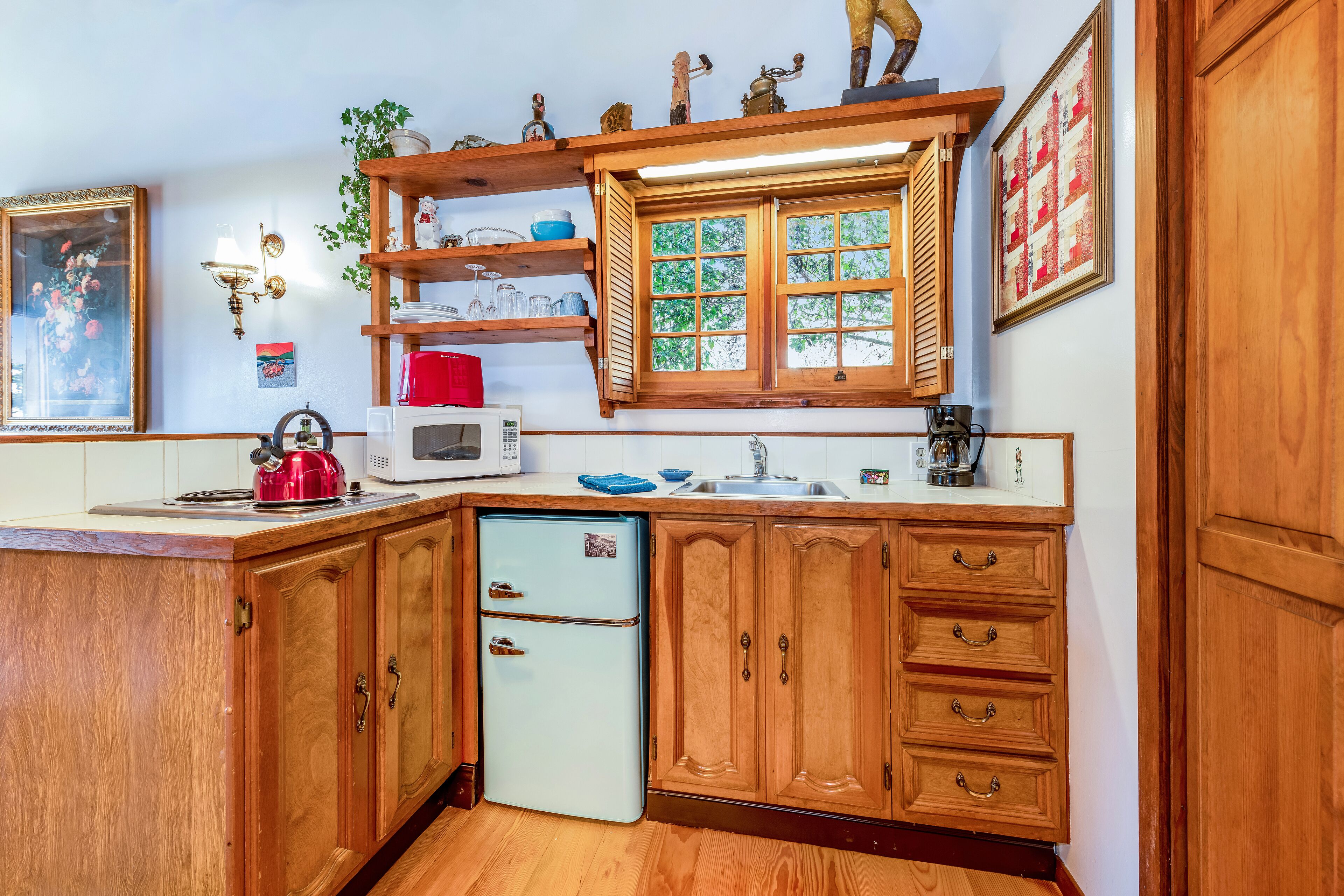 A kitchen with wooden cabinets, a built-in microwave, a refrigerator, and a window with shutters.