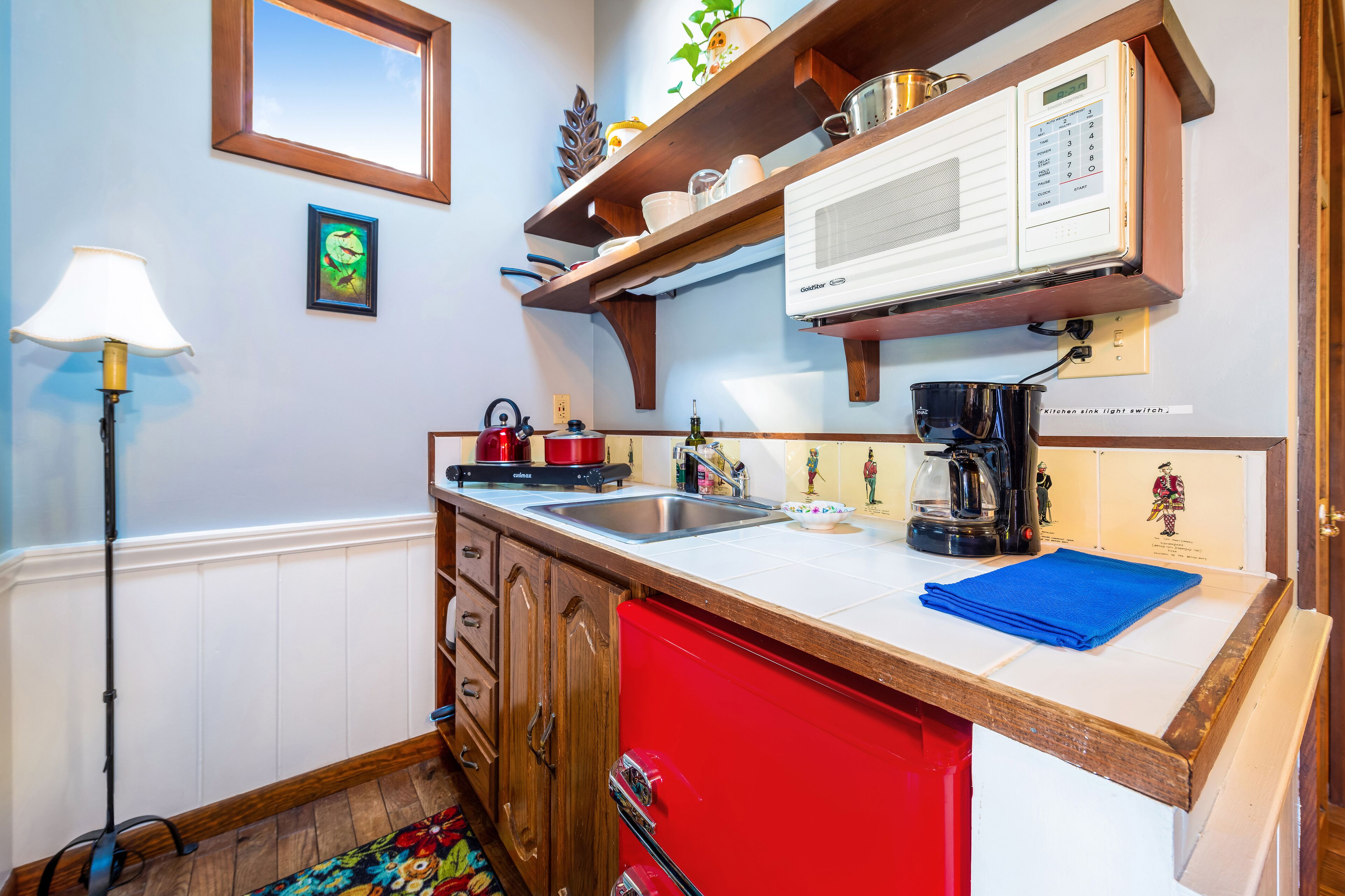 A kitchen with a red refrigerator, a microwave, and a coffee maker on the counter. There is a sink and a stove with pots and pans.